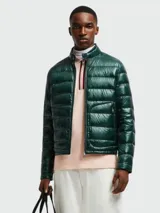 Campera corta tipo puffer de Moncler, modelo Acorus, en color verde oscuro con acabado brillante. Presenta diseño acolchado horizontal, cuello alto con cierre de broche, cierre frontal completo y bolsillos laterales con cierre.