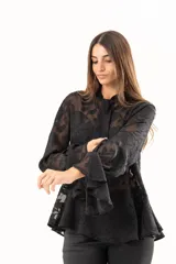 Blusa negra de tejido semitransparente con diseño floral en relieve, cuello alto con lazo frontal y mangas largas con volados en los puños.