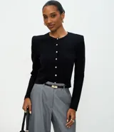 Cardigan de punto negro con cuello redondo, mangas largas y hombreras estructuradas. Presenta un cierre frontal con botones delicados y un corte regular.