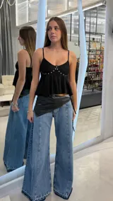 Top negro de tirantes finos, con escote en V y detalle de pedrería brillante en la parte delantera. Presenta diseño peplum con volados en la parte inferior.