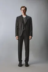 Pantalón de traje de corte regular fit confeccionado en lana de origen italiano. Presenta un diseño de cuadros sutiles, bolsillos laterales, bolsillos traseros de doble vivo con botón y cierre frontal con cremallera y botón.