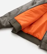 Campera bomber de poliuretano con acabado efecto cuero, cuello redondo, cierre frontal con cremallera, bolsillos delanteros y bolsillo utilitario en la manga. Presenta puños y ruedo elásticos, con forro interior en contraste.