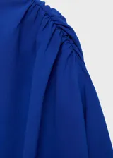 Blusa de manga larga en color azul eléctrico, con diseño asimétrico de un solo hombro con tirante fino y detalle fruncido en el hombro opuesto. Presenta un corte recto con ajuste en la cintura y cierre lateral.
