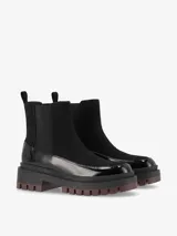 Botas Chelsea de caña baja color negro, combinadas en eco cuero charol y gamuza, con paneles elásticos laterales y suela track gruesa de goma con base dentada.