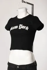 Remera de morley de manga corta, color gris, ajustada al cuerpo y elastizada, con bordado estilo college con la inscripción 'New York' en el pecho.