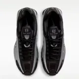 Championes Nike modelo Shox R4, con diseño futurista que combina paneles de cuero sintético negro y plateado metálico. Presenta la icónica tecnología de amortiguación Shox en el talón con columnas plateadas y el logo de Nike en el lateral.