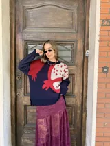 Buzo tejido de silueta oversize y calce relajado, con diseño gráfico inspirado en una granada en tonos rojo, azul marino y crema. Presenta cuello redondo, puños y ruedo acanalados.