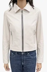 Chaqueta de cuero ovino color crema, con cuello camisero, cierre frontal con cremallera metálica y bolsillos laterales con cierre. Presenta un corte recto y estructurado.