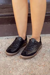 Zapatillas urbanas negras de cuero con detalles en gamuza y suela marrón con costuras blancas.