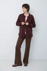 Cardigan de punto color beige, con cuello camisero, cierre frontal de botones y bolsillo aplicado en el pecho. Presenta mangas largas con puños acanalados y un corte recto y holgado.