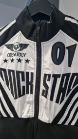 Campera corta con cierre frontal, confeccionada en una combinación de tela y apliques de cuerina, con diseño bicolor en blanco y negro, cuello alto y estampas de estilo motociclista.