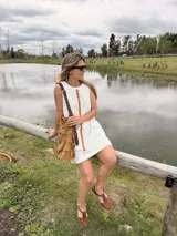Vestido corto de jean crudo, de silueta holgada y sin mangas, con una tira vertical central de cuero color camel y bolsillos laterales.
