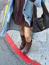 Bota biker de caña alta confeccionada en cuero vacuno color marrón con efecto desgastado. Presenta punta almendrada, taco cuadrado de madera y múltiples tiras decorativas con hebillas metálicas laterales.