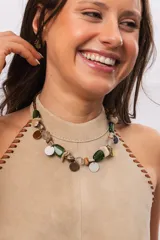 Collar corto de diseño artesanal compuesto por cuentas de cristal verde, abalorios de nácar, piedras naturales y pequeños dijes metálicos colgantes circulares en tonos dorados y plateados.