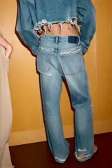 Jeans de corte boyfriend y tiro medio, con diseño de cinco bolsillos, cierre frontal con cremallera y botón metálico. Presenta un acabado lavado con detalles de roturas y desgastes.