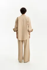 Camisa oversize de color beige claro, con cuello camisero, manga larga con puños anchos doblados y un bolsillo de parche en el pecho.