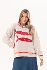 Sweater tejido color crudo con cuello redondo y mangas largas. Presenta dos peces rojos con detalles en azul bordados en el frente. Tiene ribete ondulado rojo en cuello, puños y ruedo.