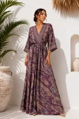 Vestido largo de estilo bata y corte cruzado, con mangas amplias y un lazo ajustable en la cintura. Presenta un estampado de diseño paisley en tonos morados, marrones y azules.