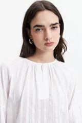 Blusa de manga larga color negro, confeccionada en 100% algodón con textura bordada. Presenta detalles de tablas en el frente y en los puños, con un corte holgado y cuello redondo con pequeña abertura.