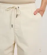 Bermuda masculina tipo runner de terciopelo cotelé, color beige, con cintura elástica, cordón ajustable y bolsillos laterales.