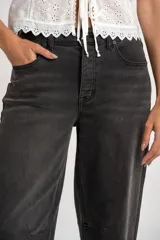 Jean de corte baggy con tiro medio, confeccionado en denim de color gris lavado. Presenta un diseño de pierna ancha con costuras horizontales a la altura de la rodilla y cierre frontal con botón y cremallera.