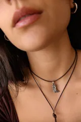 Collar de doble vuelta con cordón marrón y dije metálico en forma de bota vaquera con detalles grabados.