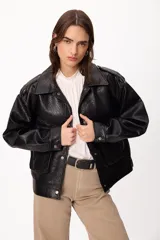 Chaqueta de cuero sintético negro con textura granulada, corte oversize, cuello camisero, cierre frontal con botones a presión, bolsillos frontales con solapa y charreteras en los hombros.