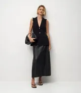 Pollera midi de corte evasé confeccionada en poliuretano con acabado que imita el cuero. Presenta cintura con trabillas, cierre frontal tradicional y solapas decorativas en la parte delantera.