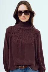 Blusa color bordó con cuello alto fruncido y mangas largas abullonadas con puños elásticos.