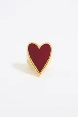 Anillo de metal dorado con un dije grande en forma de corazón relleno de material rojo con glitter.