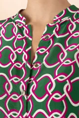 Camisa verde con estampado de cadenas entrelazadas en tonos verde oscuro, blanco y fucsia, de mangas cortas y cuello camisero.