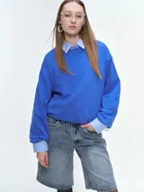 Buzo oversize de color azul vibrante, con cuello redondo acanalado, mangas largas anchas y bajo regulable mediante elásticos laterales.