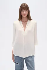 Blusa de poliéster color blanco, con cuello en V y mangas 3/4. Presenta un diseño holgado con un pliegue central en el frente y un acabado satinado.