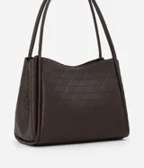 Cartera modelo hobo de gran tamaño, confeccionada en poliuretano con textura geométrica triangular. Presenta asas tubulares largas para llevar al hombro, cierre superior con cremallera y un pequeño aplique metálico dorado en la parte frontal.