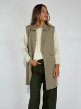 Chaleco largo color beige, con cuello solapa, un botón frontal y dos bolsillos de parche. Presenta costuras decorativas en contraste.