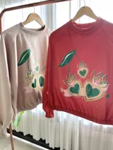 Buzo cropped de algodón color rojo con estampa frontal exclusiva de corazones con diseño de cerezas y hojas, manga larga y cintura elastizada.