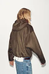 Chaqueta bomber de efecto ante en color marrón, con capucha ajustable mediante cordones, cierre frontal con cremallera, bolsillos laterales y bajo con elástico interior.