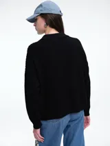 Sweater de tejido de punto color beige, con diseño de trenzas en el frente y mangas lisas. Presenta cuello polo con escote en V y puños y ruedo acanalados.