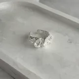 Anillo plateado con diseño irregular y abertura ajustable.