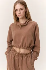Buzo cropped de cuello alto con cordón regulable, mangas largas con puños elásticos y cintura ajustable con cordón. Presenta un diseño moderno y versátil con acabado suave.