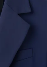 Blazer azul marino de estilo sastrero, corte recto, con cuello pico y solapas de muesca. Cuenta con dos bolsillos con solapa en los laterales y cierre frontal de doble botonadura.
