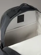 Mochila negra de poliéster con diseño moderno y funcional. Presenta un compartimento principal con cierre, bolsillos exteriores con cremallera en el frente, laterales y espalda, y correas acolchadas. En el bolsillo frontal se destaca el logo de Calvin Klein en blanco con la inscripción "West 39th Street New York City".