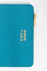 Billetera compacta de estructura blanda en color turquesa, con cierre de cremallera superior y logo metálico dorado en el frente.