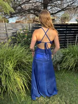 Vestido largo sin mangas con escote en V halter y aberturas laterales (cut-outs) en la cintura. El cuerpo superior presenta un llamativo diseño estampado multicolor, mientras que la falda larga es de tejido texturizado brillante en color verde esmeralda con inserciones godet en el ruedo.