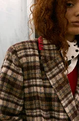 Blazer sastrero de corte oversize, con cuello solapa, manga larga y cierre frontal con botones. Presenta un diseño a cuadros en tonos bordó y blanco, con detalles de costuras bordadas en hilo amarillo en los bolsillos y el ruedo. Incluye forro interior de satén.