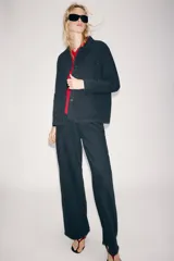 Chaqueta oversize de mezclilla color azul marino, de cuello solapa y manga larga, con bolsillos de parche en el delantero y cierre frontal con botones metálicos.