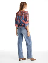 Blusa de gasa con estampado de arabescos en tonos azules y rojos, con cuello a la base y mangas tipo capa. Presenta una silueta holgada con ruedo elástico en punto smock que ajusta a la cintura.