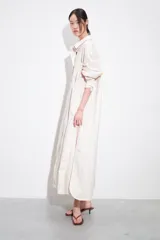 Vestido camisero largo de manga larga, color blanco con finas rayas verticales en tono claro, con cuello solapa y abotonadura frontal. Posee un calce amplio y bolsillos laterales.