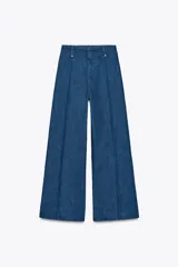 Jeans de tiro alto y pierna ancha de Zara, confeccionados en mezcla de algodón color beige. Presentan cintura con trabillas, bolsillos de parche en la espalda, costuras frontales marcadas y cierre delantero con cremallera, botón y gancho metálico.