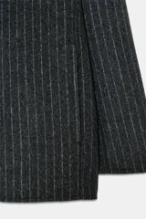 Blazer de corte recto confeccionado en mezcla de lana con estampado de rayas verticales. Presenta cuello redondo con bufanda incorporada en el mismo tejido, manga larga, bolsillos delanteros y cierre frontal con botones.